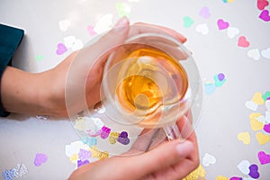 Top view of hands of a girl holding a transparent cup with green tea sitting near table. Bright highlights on a glass. Cozy