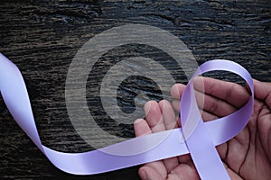 Top view of hands holding lavender or light purple orchid color ribbon on dark wooden background. General and testicular cancer