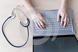 Top view of hands on the keyboard. Woman doctor at the desk typing on a laptop. A nurse fills out a patients electronic