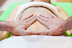 Top view of hands massaging female abdomen. Therapist applying pressure on belly. Woman receiving massage at spa salon