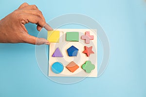 Top view Hands Picking up one Colorful Wooden building blocks in different shapes on blue background.