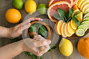 Top view hands pounding mint with pestle in mortar, citrus on dish