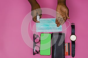 Top view of hands with sanitizer, phone, mask, watch, credit card, wallet, and eyeglasses