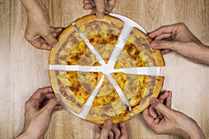 Top view of hands taking slices of delicious and crispy hawaiian pizza. Group of hungry friends sharing delicious lunch on wooden