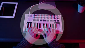 Top view of hands using midi keyboard in home studio with neon lights