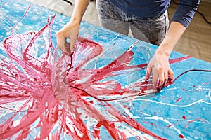 Top view of hands of woman stained with red paint painting with rope abstract picture of flower on blue, white canvas.