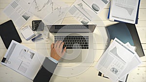 Top view hands of young businessman typing text on laptop keyboard at white desk and drinking coffee. Male arms of