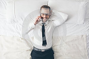 Top view. Handsome businessman with glasses on bed calling from his phone