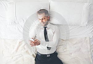 Top view. Handsome businessman lying on bed texting from his smartphone