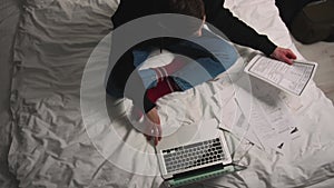 Top view. Handsome man working with Documents using laptop on Bed before going to sleep at home. Man working with papers