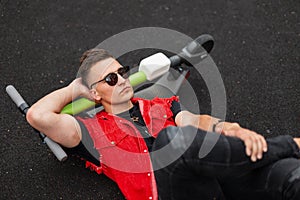 Top view of a handsome young hipster man in vintage denim red-black clothes in sunglasses with a stylish hairstyle outdoors.