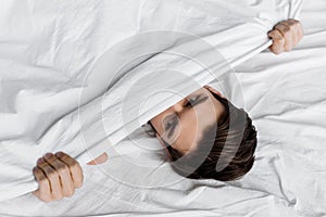 Top view of handsome young man hiding under blanket in bed