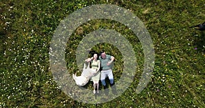 Top view at the happy beautiful loving couple lying on the meadow and petting two lovely dogs. The handsome man is