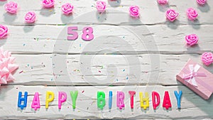 Top view of happy birthday 58 candle letters for a girl in pink shades with beautiful rose flowers, postcard congratulation copy