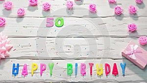 Top view of happy birthday 50 candle letters for a girl in pink shades with beautiful rose flowers, postcard congratulation copy