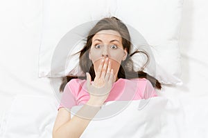 Top view of happy brunette young woman lying in bed with white sheet, pillow, blanket. Female spending time in room