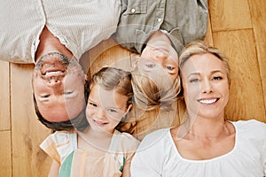 Top view of happy caucasian family lying together on the wooden floor at home. Portrait of a mature couple bonding with