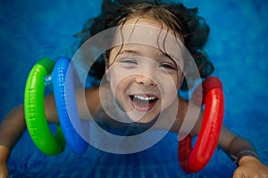 Top view of happy child wearing inflatable armbands playing in swimming pool. Summer vacation concept.