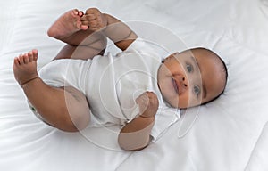 Top view of Happy cute little African newborn baby lying down smiling and looking at camera on white bed in bedroom at home