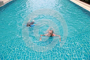 Top view happy elderly caucasian husband and elderly asian wife swimming in pool during retirement holiday with relaxation on