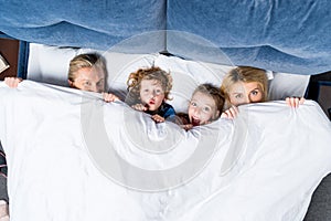 top view of happy family with two kids lying under blanket