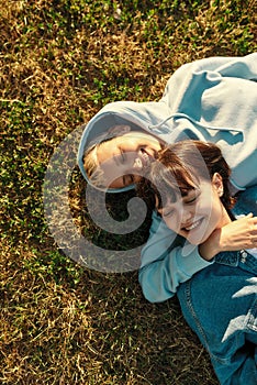 Top view of happy lesbian couple of girls lying on the grass in summer park, women in love laughing, spending time