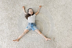 Top view happy little girl relaxing on carpet at home