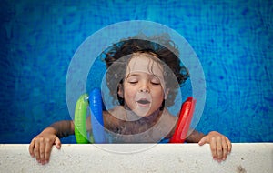 Top view of happy little girl wearing inflatable armbands learning to swim in swimming pool. Summer vacation concept.