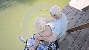 Top view of a happy mature couple sitting on the bench near the river, admiring nature. Senior woman kissing her husband