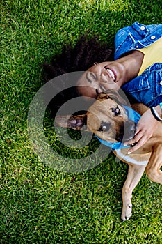Top view of happy multiracial teenage girl with her dog lying in the grass. Concept of relationship between dog and