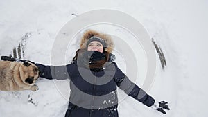TOP view: Happy woman making snow angels, her pug dog running and jumping around