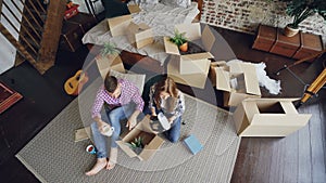 Top view of happy young couple unpacking things, opening box, taking things and talking after moving to new apartment