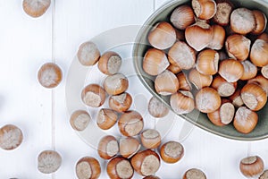 top view of hazelnuts in a bowl and scattered on white wooden background
