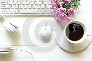 Top view headphones on white desk and computer with pink flower and copyspace area for a text and Cup of coffee beside headset.