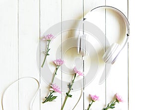Top view headphones on white desk with pink flower and copyspace area for a text