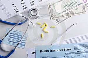 Top view of health insurance card, plans, cash, pills, stethoscope and calendar on the white table. Concept of health care and pay