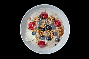 Top view of healthy cereal and oatmeal breakfast with berries and nuts in a white bow