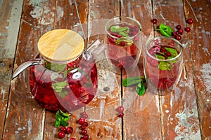 Top view of healthy detox water drinks with cranberries in glass jars with drinking straw on kitchen table with ingredients.