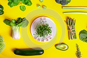 Top view healthy raw vegetables on yellow background, white plate with sprouts and Go vegan message on wooden blocks. Vegetarian