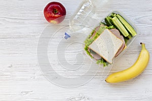 Top view, healthy school lunch box with sandwich, fruits and bot