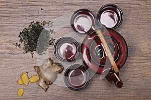 Top view of heap of dry green tea, fresh ginger and chinese tea set on the wooden surface