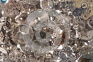 Top view of heap of metal internal parts of an old clock on a white light background. Silver clockwork with gears and