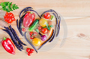 Top view of a heart made from pods of asparagus beans and fresh ripe vegetables on a wooden table