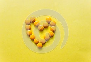 top view of heart made from yellow pillows of dietary supplements on yellow background. copy space. Concept of healthy life,