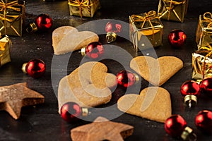 Top view of heart shaped gingerbread cookies on dark wooden table with red baubles and golden Christmas packets