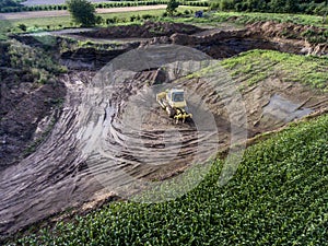 Top view heavy machine excavator bagger working in mud on construction site with green landscape surrounding