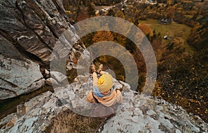 Top view hiker man with backpack sitting in cliff and enjoying fall landscape in valley