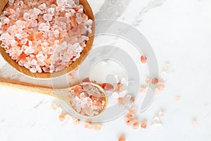 Top view of himalayan pink rock salt in wooden bowl and spoon on white marble table
