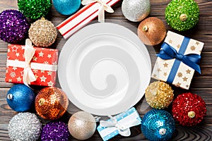 Top view of holiday setting on wooden background. Plate, gifts, baubles and Christmas decorations. New Year dinner concept