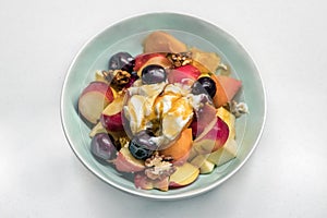 Top view of a home made greek fruit salad with nuts, apple, peach, grapes and yogurt with honey.
